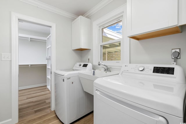 clothes washing area with crown molding, washing machine and dryer, cabinet space, baseboards, and light wood-style flooring