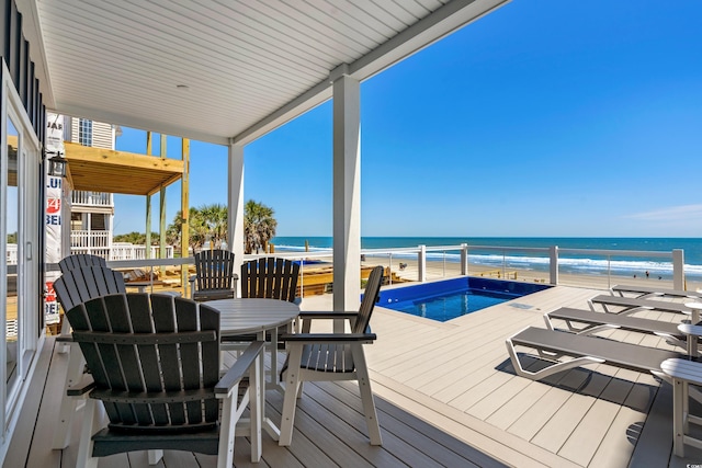 wooden terrace with a pool, a water view, a view of the beach, and outdoor dining space