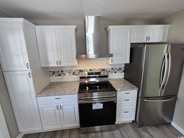 kitchen featuring wall chimney range hood, wood finished floors, white cabinetry, decorative backsplash, and appliances with stainless steel finishes