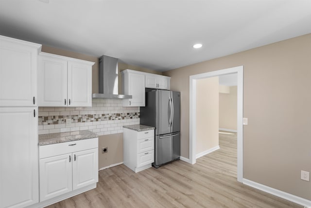 kitchen with freestanding refrigerator, wall chimney exhaust hood, light wood-style flooring, decorative backsplash, and white cabinets