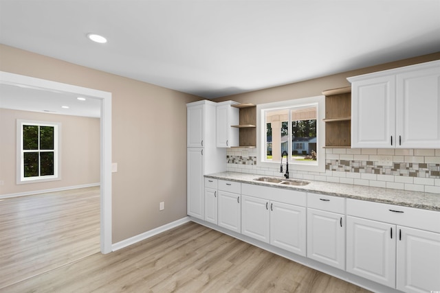 kitchen with light wood-style flooring, baseboards, a sink, open shelves, and decorative backsplash