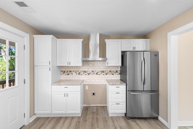kitchen featuring freestanding refrigerator, visible vents, wall chimney exhaust hood, light wood-style flooring, and white cabinets