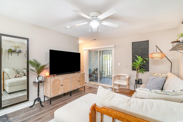 living room with a textured ceiling, a ceiling fan, baseboards, wood finished floors, and visible vents