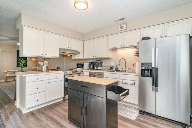 kitchen featuring visible vents, light wood-type flooring, under cabinet range hood, a sink, and stainless steel appliances