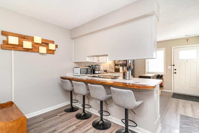 kitchen with a kitchen breakfast bar, baseboards, wood finished floors, and white microwave