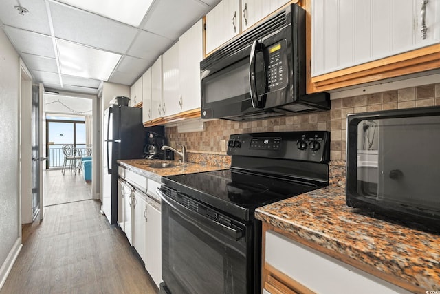 kitchen featuring white cabinets, a sink, wood finished floors, tasteful backsplash, and black appliances