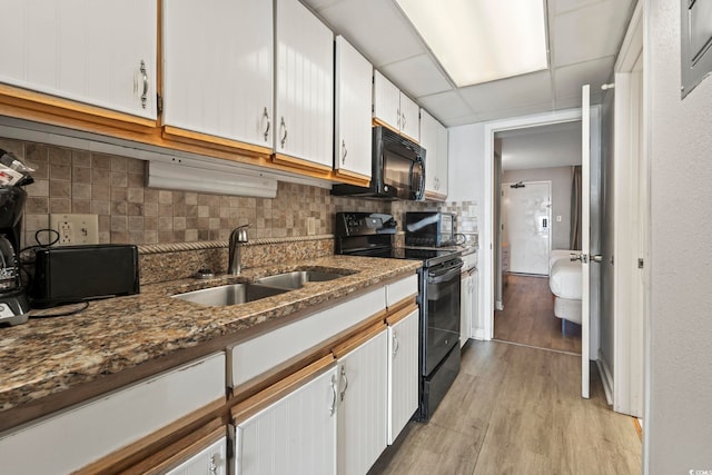 kitchen with white cabinetry, tasteful backsplash, a sink, light wood-style flooring, and black appliances