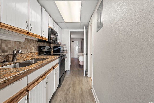 kitchen with tasteful backsplash, a sink, baseboards, black appliances, and light wood-style flooring