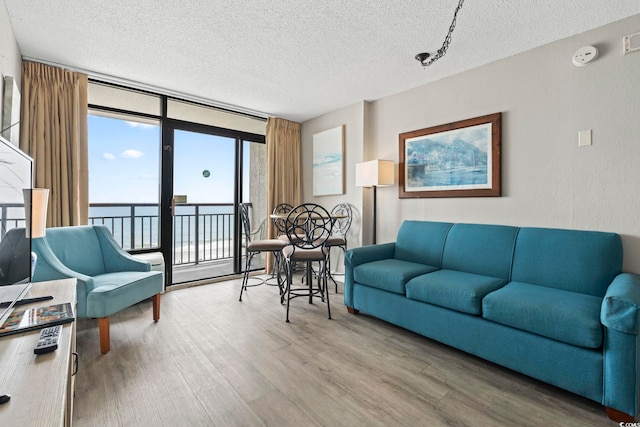 living room with a textured ceiling, a water view, wood finished floors, and a wall of windows