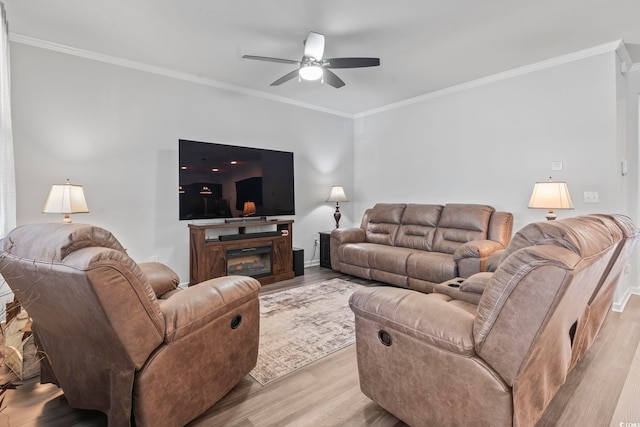 living room with a ceiling fan, a glass covered fireplace, ornamental molding, and light wood finished floors