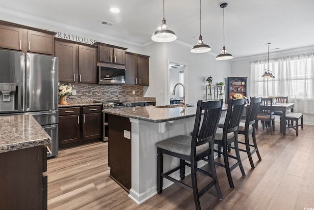 kitchen featuring appliances with stainless steel finishes, a sink, a breakfast bar area, backsplash, and ornamental molding