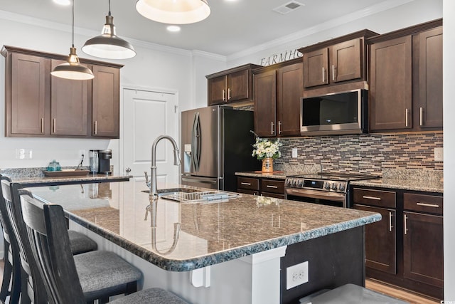 kitchen with dark brown cabinetry, appliances with stainless steel finishes, a sink, decorative backsplash, and a kitchen bar