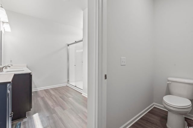 full bath featuring a stall shower, wood finished floors, vanity, baseboards, and toilet