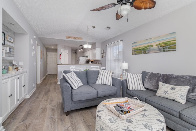 living room featuring visible vents, lofted ceiling, baseboards, light wood-type flooring, and a ceiling fan