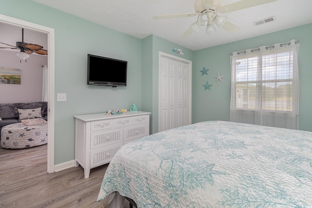 bedroom featuring ceiling fan, baseboards, wood finished floors, visible vents, and a closet