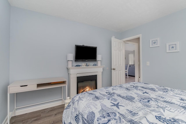 bedroom featuring baseboards, wood finished floors, and a lit fireplace