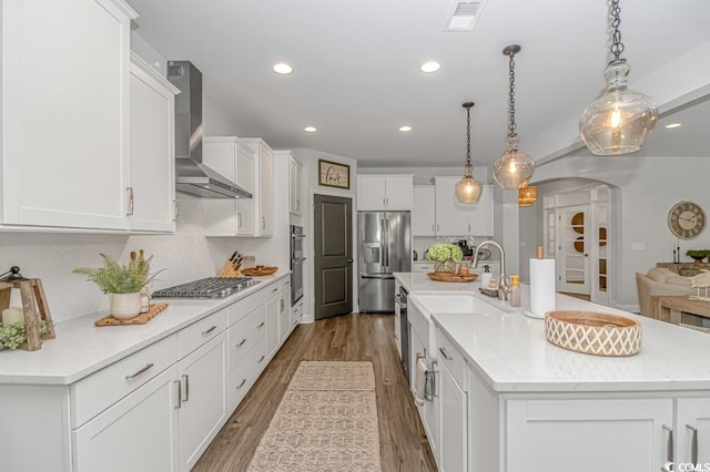 kitchen featuring decorative backsplash, visible vents, appliances with stainless steel finishes, arched walkways, and wall chimney exhaust hood