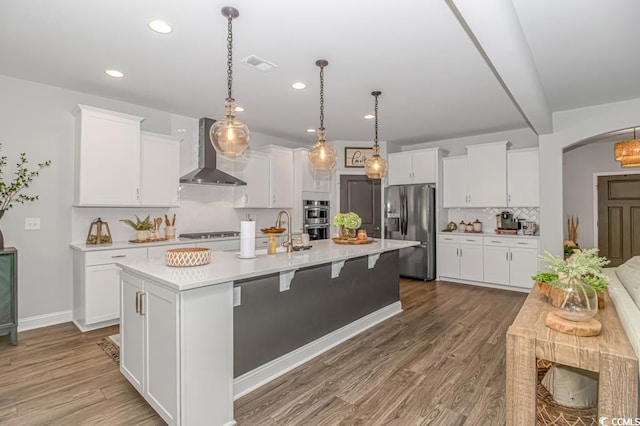 kitchen featuring light countertops, wall chimney exhaust hood, stainless steel appliances, tasteful backsplash, and visible vents