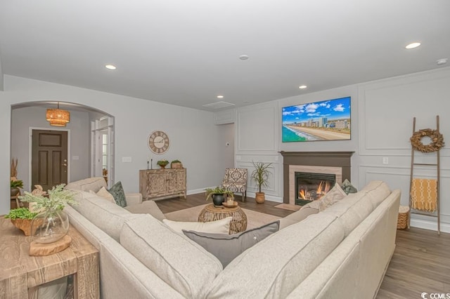 living room featuring arched walkways, a fireplace with flush hearth, wood finished floors, and recessed lighting