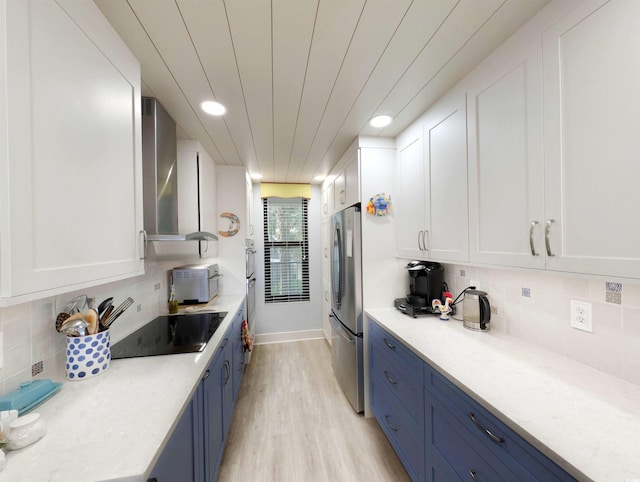 kitchen with freestanding refrigerator, white cabinetry, blue cabinetry, and wall chimney exhaust hood