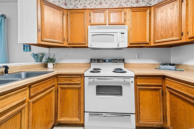 kitchen with white appliances, brown cabinetry, a sink, and light countertops