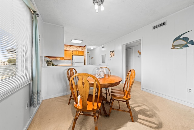 dining space with light colored carpet, a textured ceiling, visible vents, and baseboards