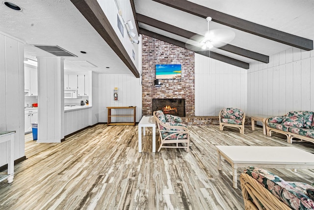living room with ceiling fan, a fireplace, lofted ceiling with beams, light wood finished floors, and wooden walls