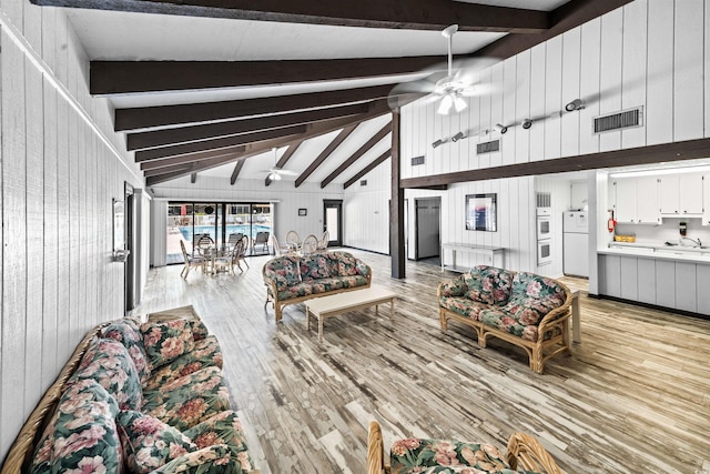 living area featuring light wood-style floors, ceiling fan, beamed ceiling, and visible vents