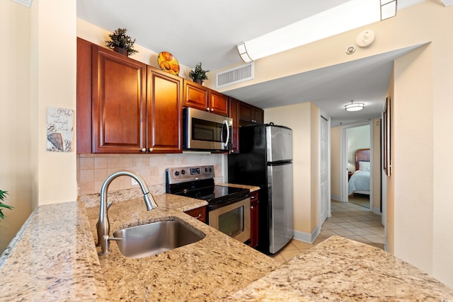 kitchen with light stone counters, a sink, stainless steel appliances, decorative backsplash, and visible vents