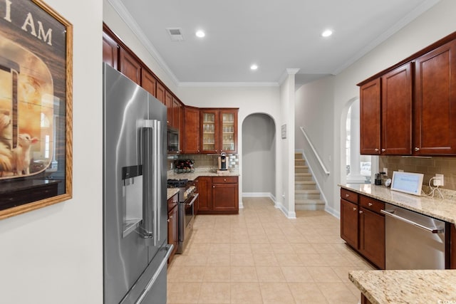 kitchen featuring crown molding, arched walkways, backsplash, premium appliances, and visible vents