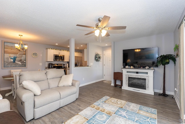living area featuring a textured ceiling, ceiling fan with notable chandelier, recessed lighting, baseboards, and wood finished floors