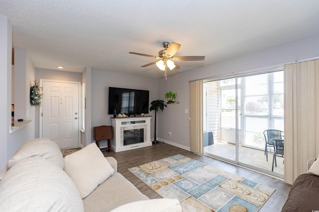 living room with a ceiling fan, wood finished floors, baseboards, a glass covered fireplace, and recessed lighting