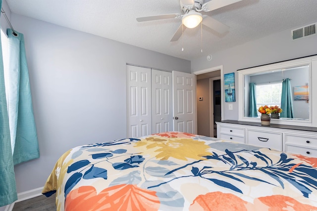 bedroom with ceiling fan, visible vents, wood finished floors, baseboards, and a closet