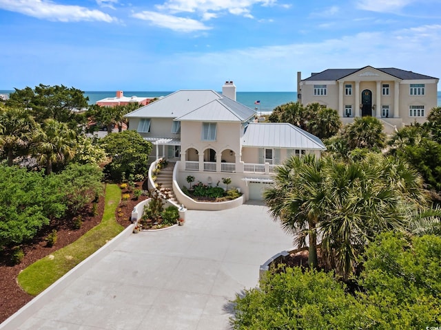 view of front of property with metal roof, curved driveway, a water view, stairs, and stucco siding