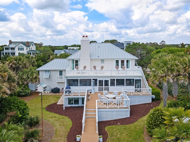 rear view of property with a standing seam roof, a chimney, a sunroom, stairway, and a balcony