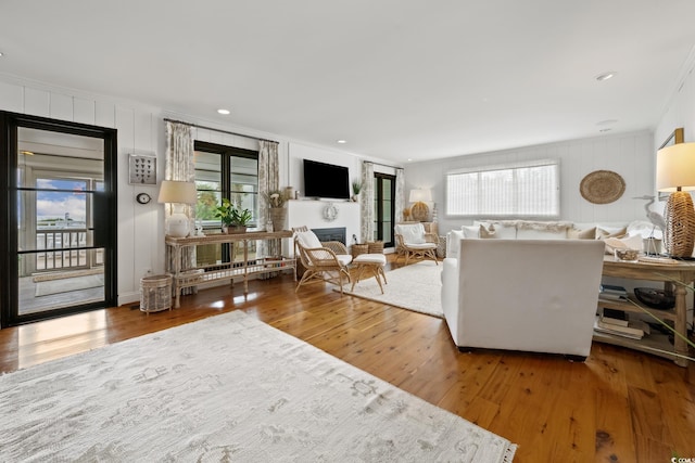 living room with crown molding, a glass covered fireplace, wood finished floors, and a healthy amount of sunlight