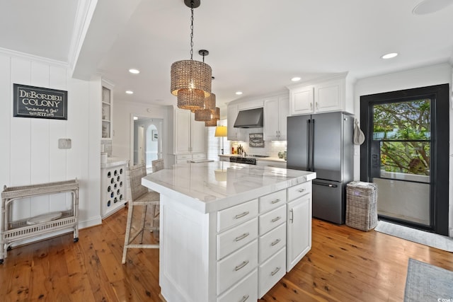 kitchen featuring freestanding refrigerator, ornamental molding, light wood-style floors, white cabinetry, and exhaust hood