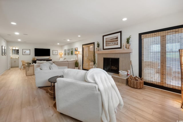 living room with a fireplace with raised hearth, recessed lighting, and light wood-style floors