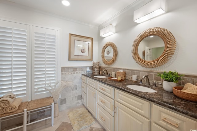 full bath with double vanity, a sink, crown molding, and tile walls