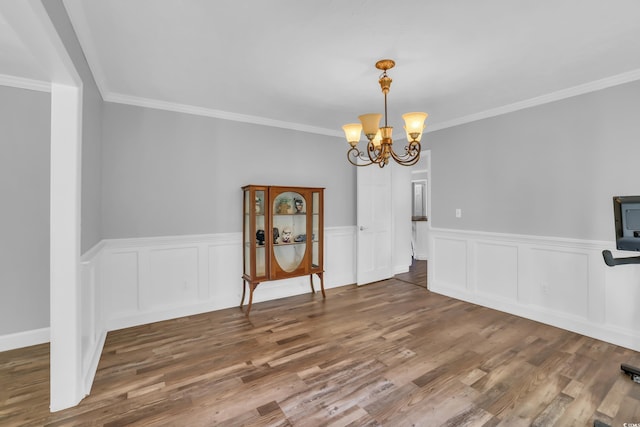 dining area featuring crown molding, a chandelier, wood finished floors, and a wainscoted wall