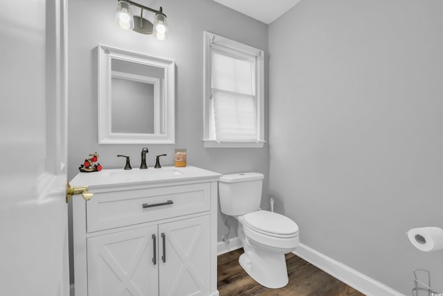 half bathroom with toilet, baseboards, wood finished floors, and vanity