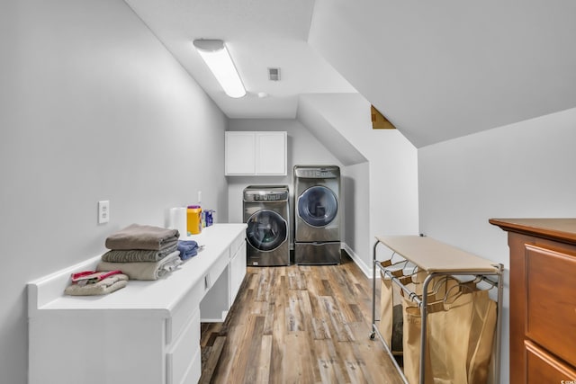 clothes washing area featuring separate washer and dryer, light wood-type flooring, and cabinet space