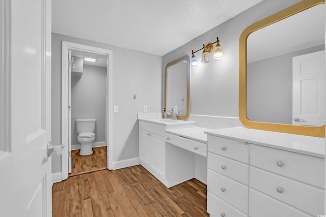bathroom with vanity, baseboards, wood finished floors, and toilet