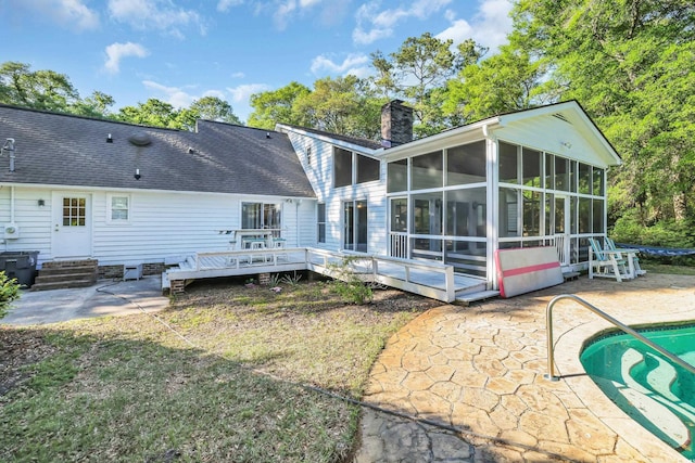 back of property with a sunroom, a patio area, a chimney, and a deck