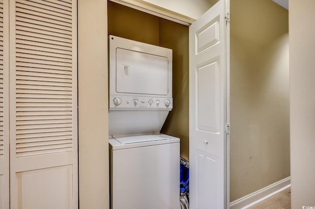 laundry area with laundry area, stacked washer and clothes dryer, baseboards, and wood finished floors