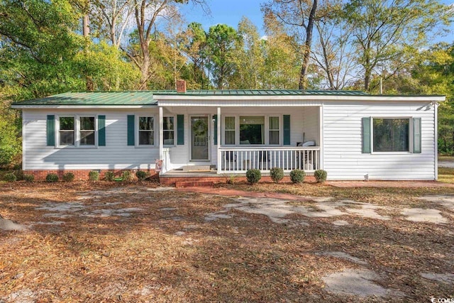 ranch-style house featuring covered porch, a chimney, and metal roof