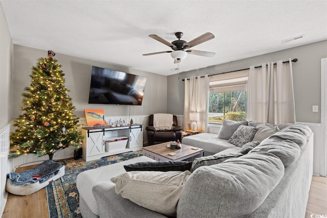 living area featuring visible vents, wainscoting, wood finished floors, ceiling fan, and a textured ceiling