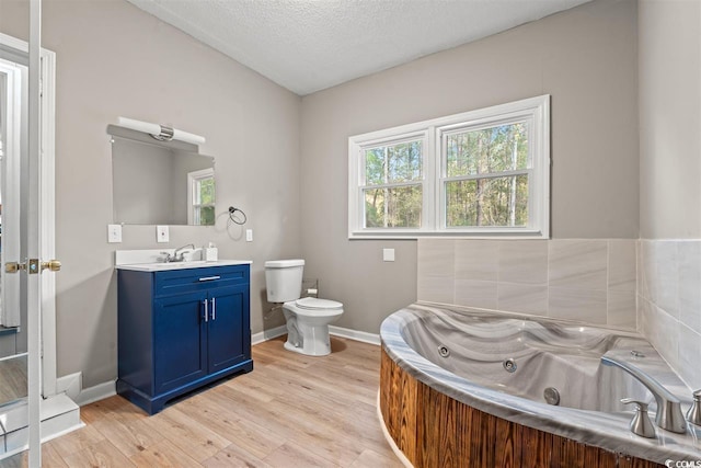 full bath with wood finished floors, vanity, baseboards, a whirlpool tub, and toilet