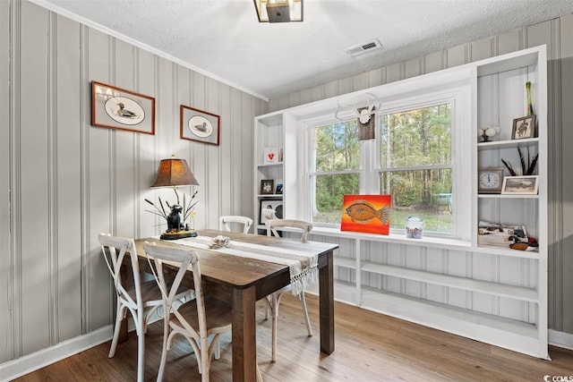 dining room with crown molding, visible vents, wood finished floors, baseboards, and a textured ceiling