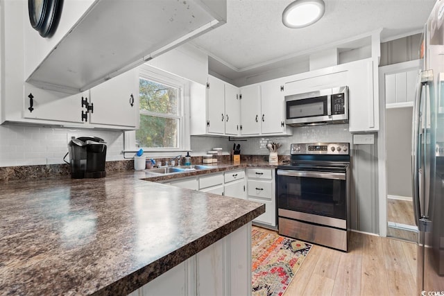 kitchen with dark countertops, white cabinetry, a sink, appliances with stainless steel finishes, and backsplash